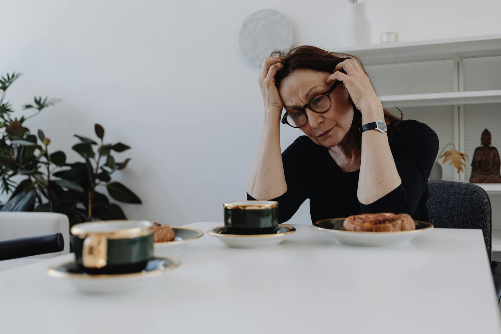 A woman sits alone at a table, expressing sadness and grief in a quiet home setting.