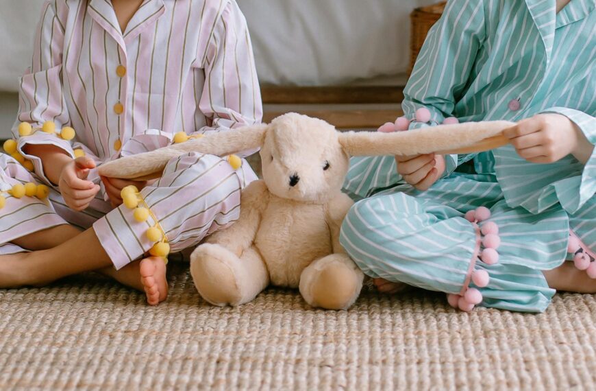 Two children in pajamas playing with a plush bunny toy, sitting together indoors.