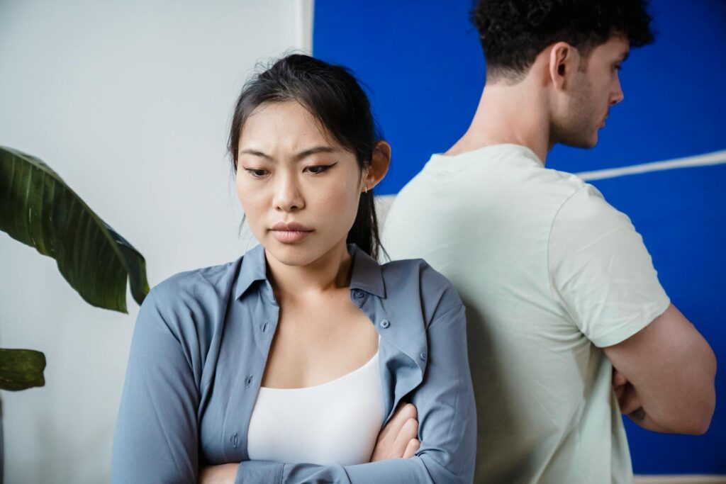 A couple in disagreement standing back to back with crossed arms, indoors.
