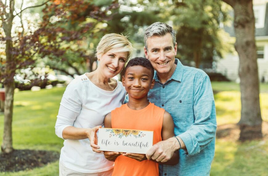 A joyful family portrait with parents and their adopted child holding a 'life is beautiful' sign.