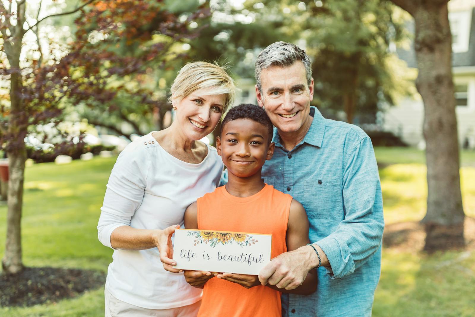 A joyful family portrait with parents and their adopted child holding a 'life is beautiful' sign.