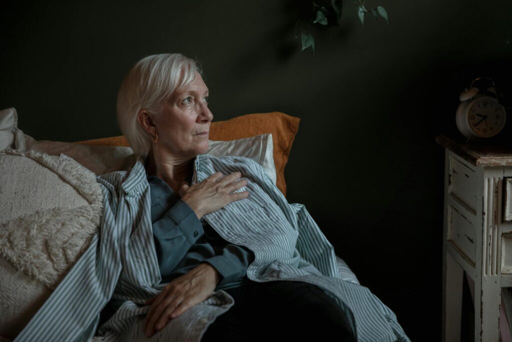A senior woman with white hair looks contemplative while reclining at home, conveying introspection and calm.