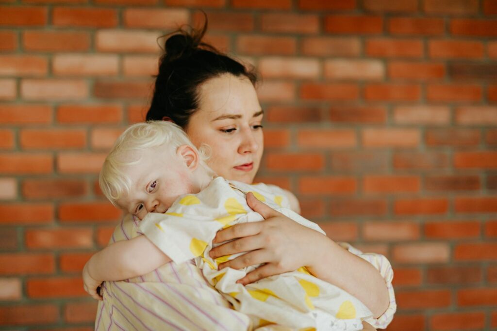 A loving mother embraces her child against a brick wall indoors, symbolizing warmth and care.