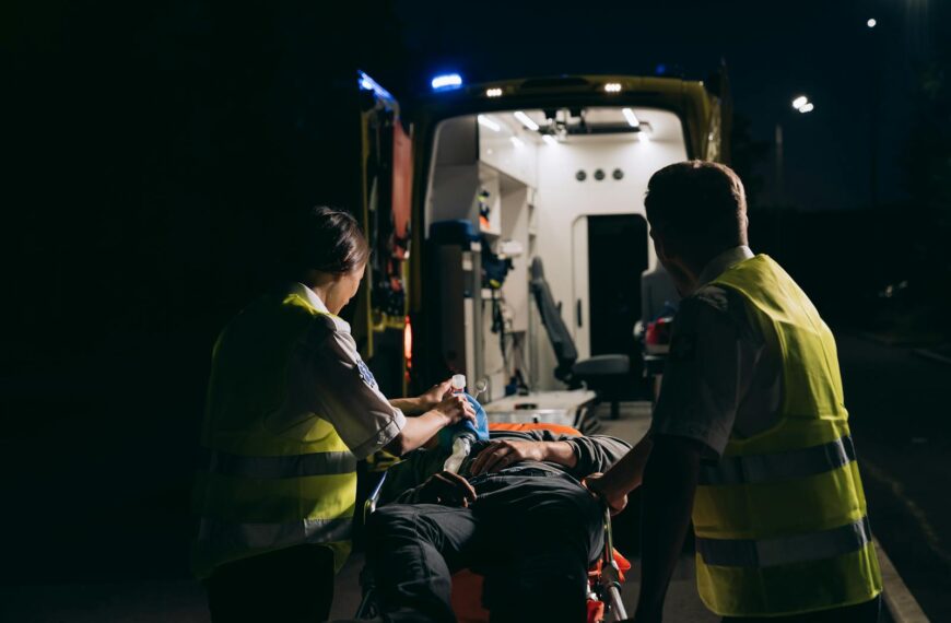 Paramedics aid patient into ambulance during night emergency.