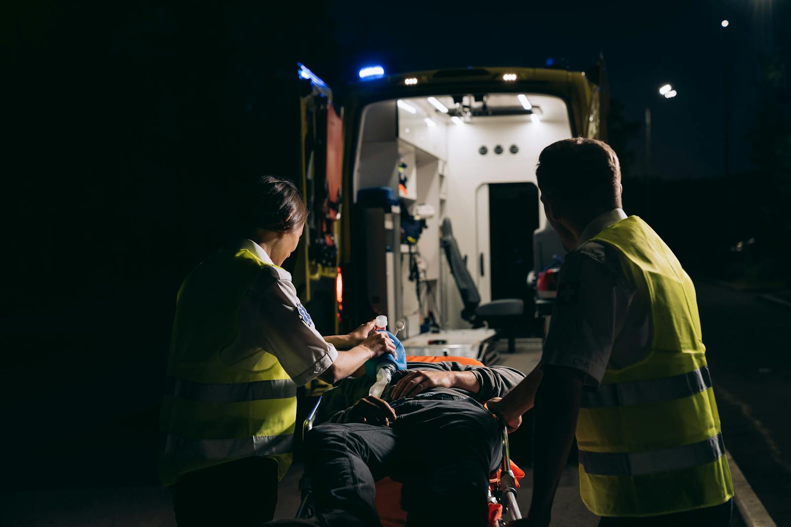 Paramedics aid patient into ambulance during night emergency.