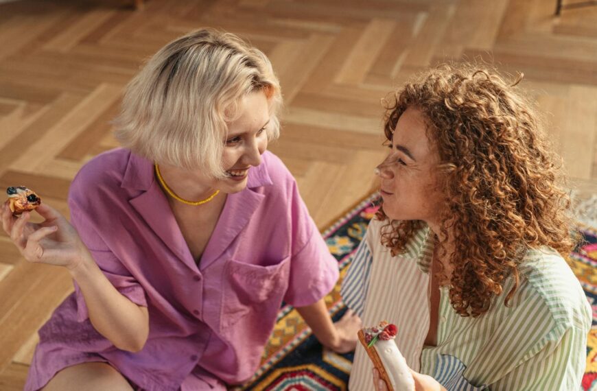 Two women sitting on the floor indoors, sharing desserts and enjoying a warm conversation.