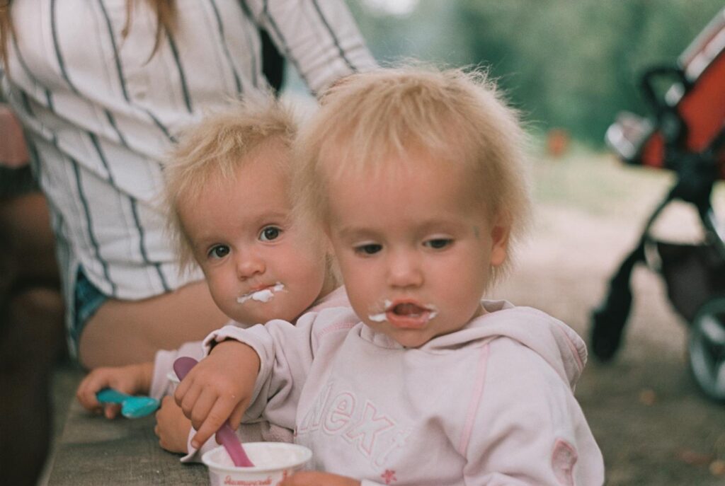 Adorable twin toddlers in hoodies enjoying ice cream together outdoors on a sunny day.
