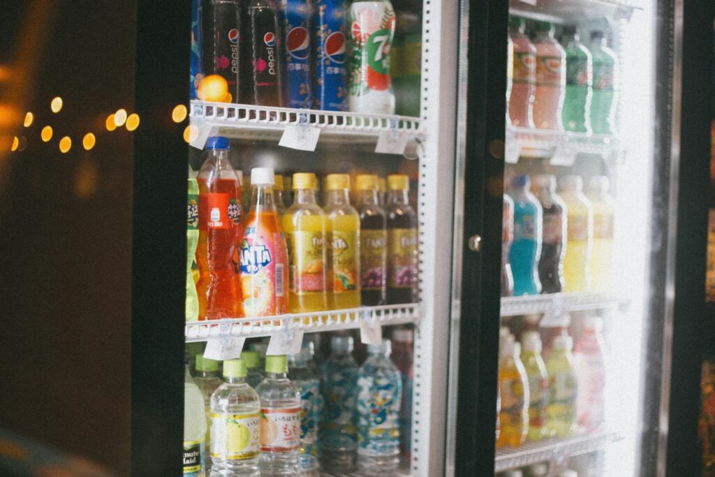 Assorted bottles of soft drinks in a commercial refrigerator with glass doors.