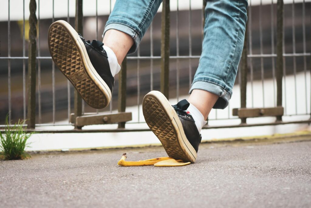 Close-up of a person slipping on a banana peel, wearing sneakers and jeans on a street.