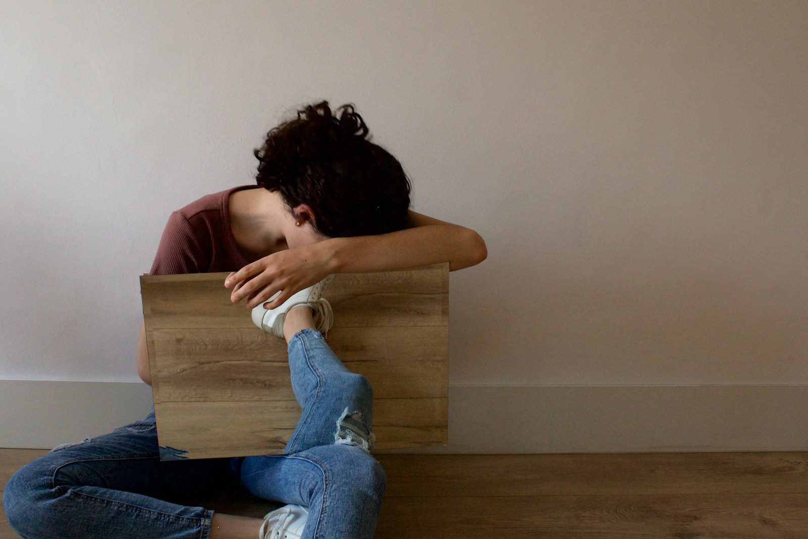 woman in red shirt and blue denim jeans sitting on brown wooden bench