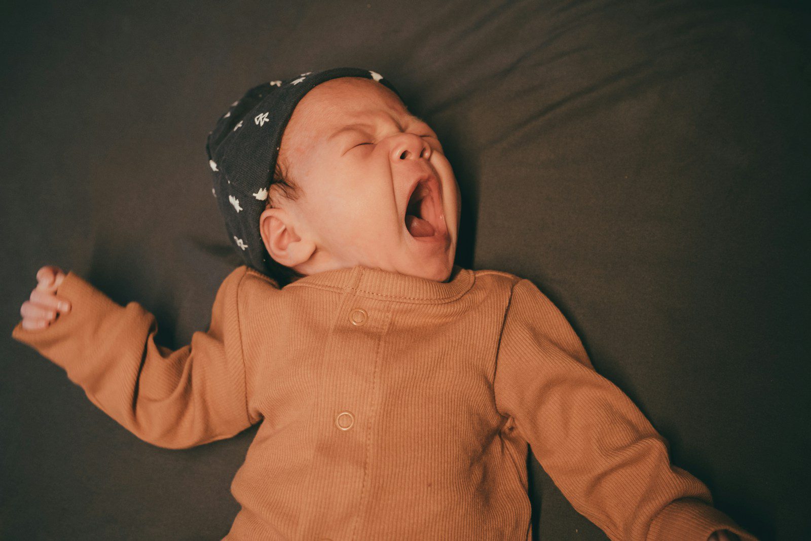 a baby yawns while laying on a bed
