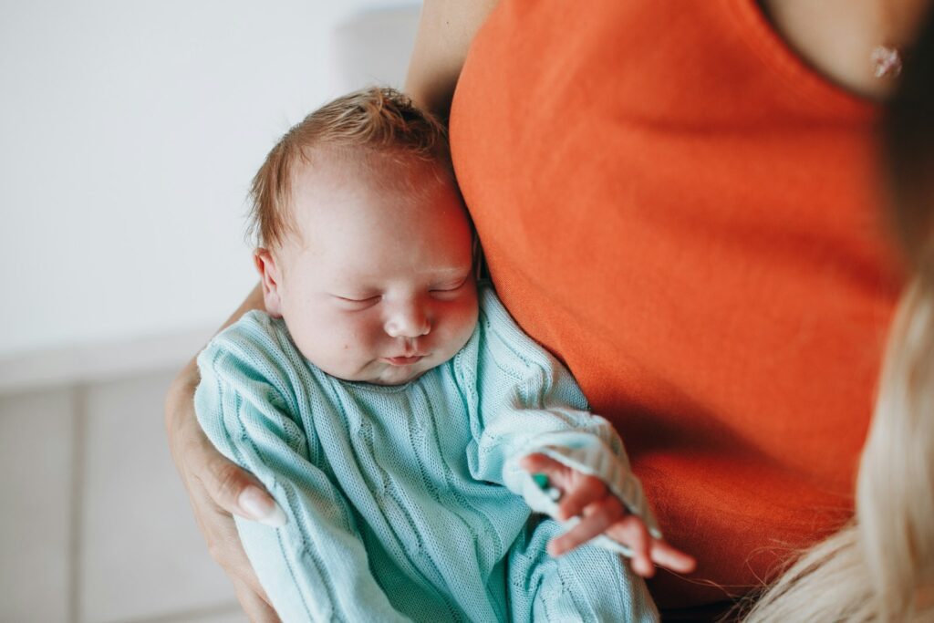 baby in green and white stripe onesie lying on orange textile