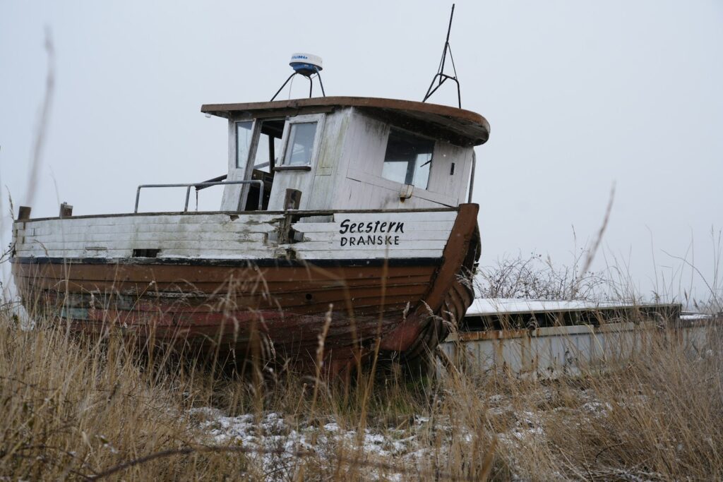 An old, weathered boat sits abandoned in dry grass.