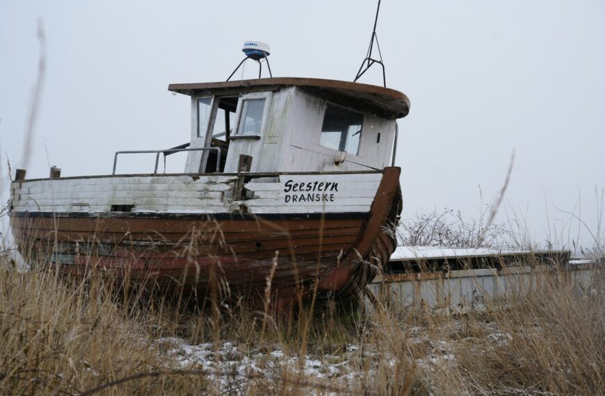 An old, weathered boat sits abandoned in dry grass.