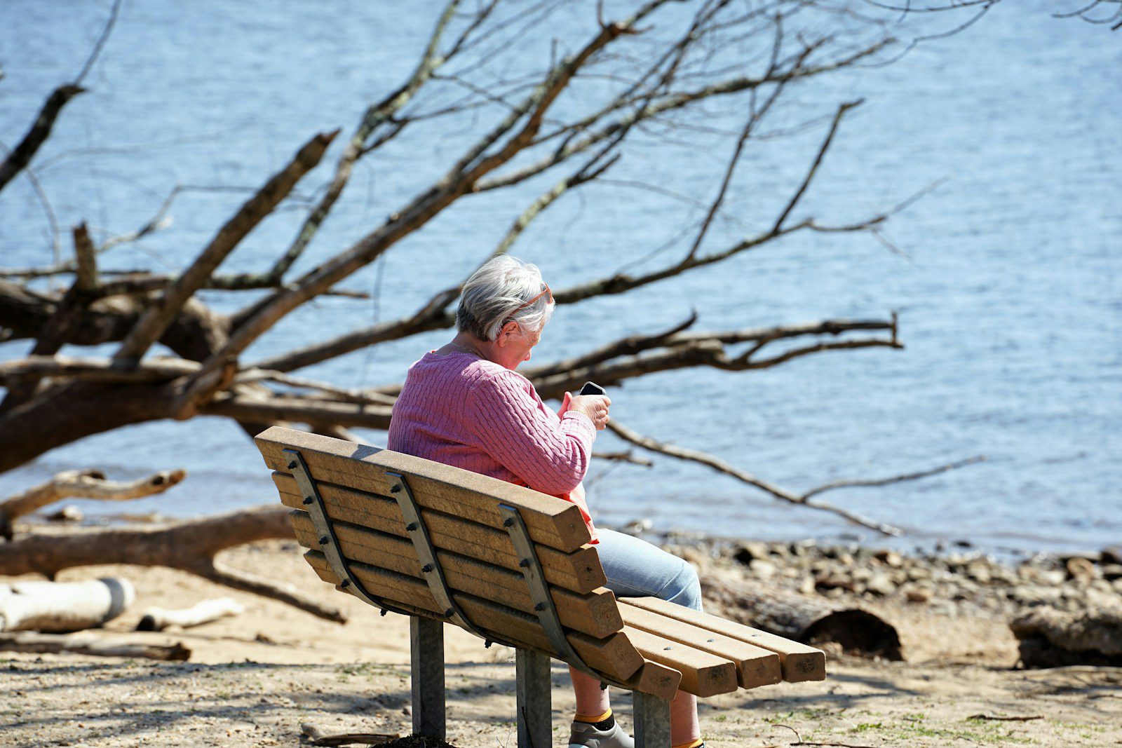 woman in pink shirt sitting on brown wooden bench near body of water during daytime