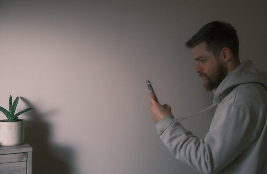 a man holding a cell phone next to a plant