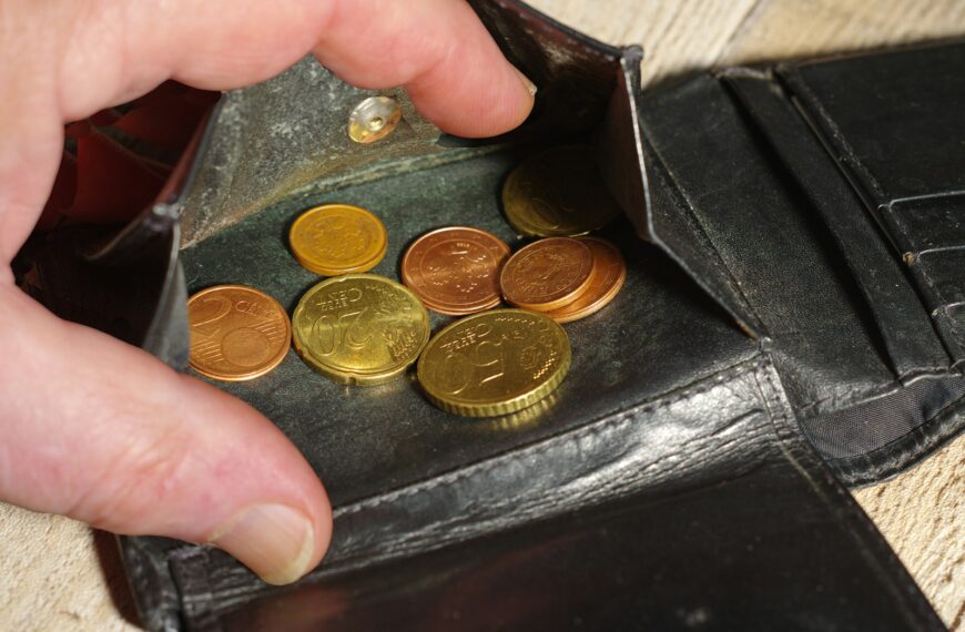 Hand placing coins into a black leather wallet.