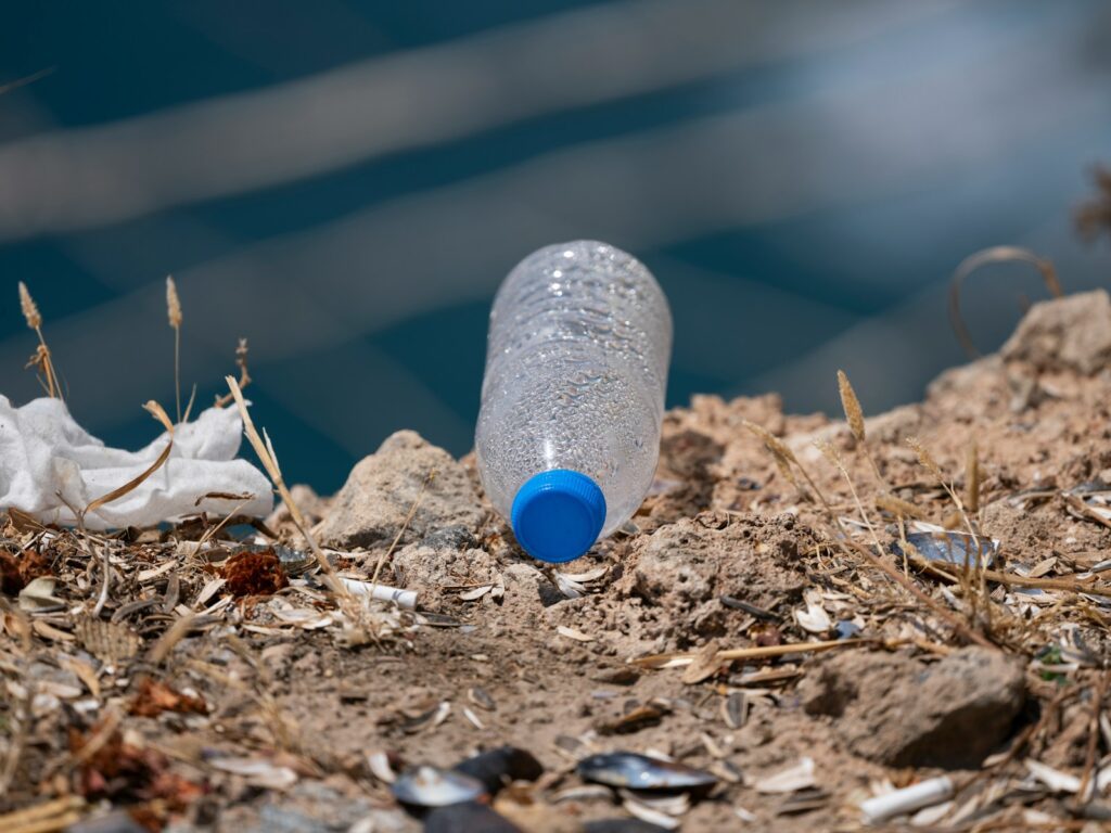 A plastic bottle lies on the ground near water.