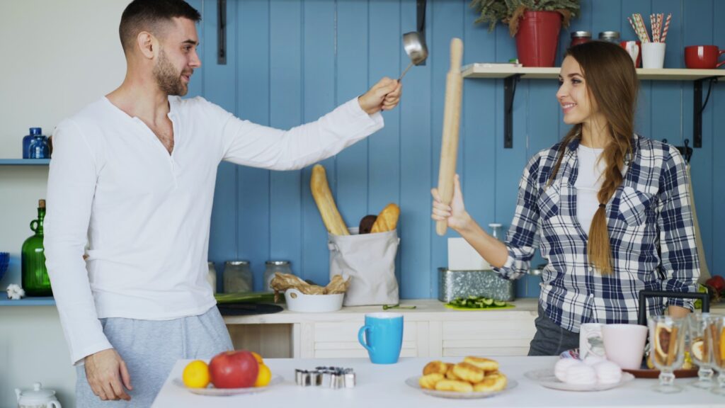 Couple playfully fighting with rolling pin in kitchen