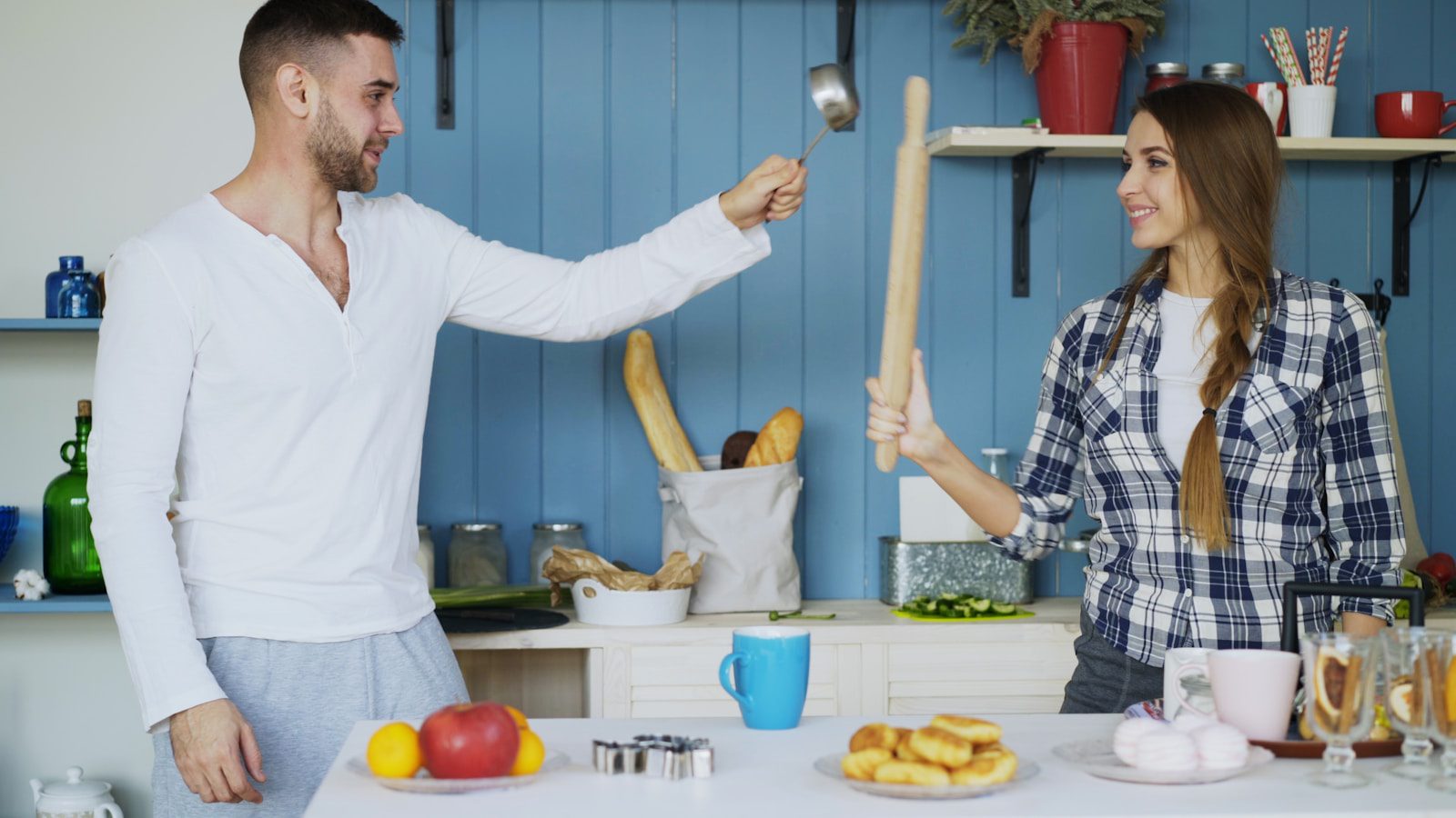 Couple playfully fighting with rolling pin in kitchen