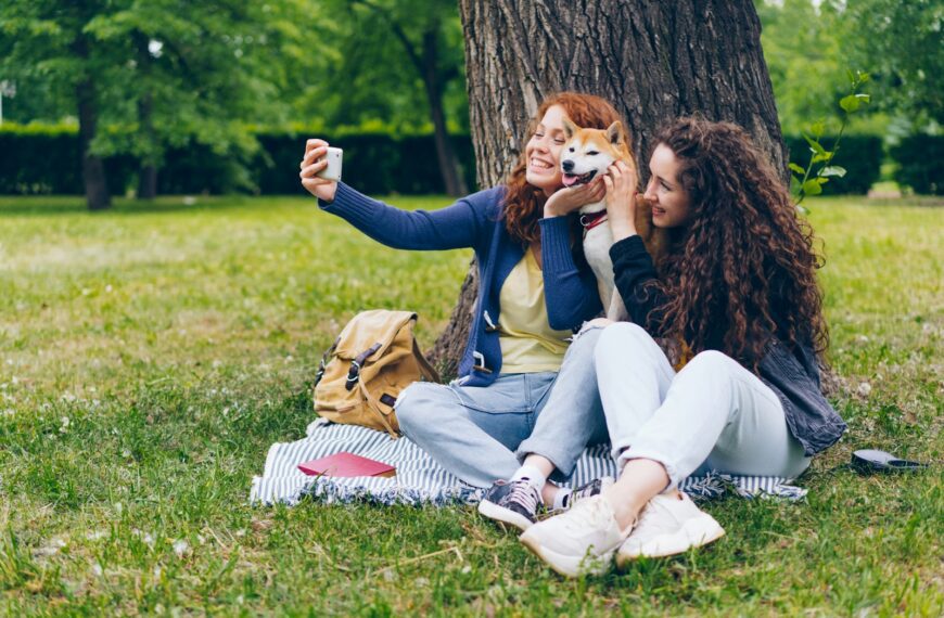two women sitting in the grass with a dog