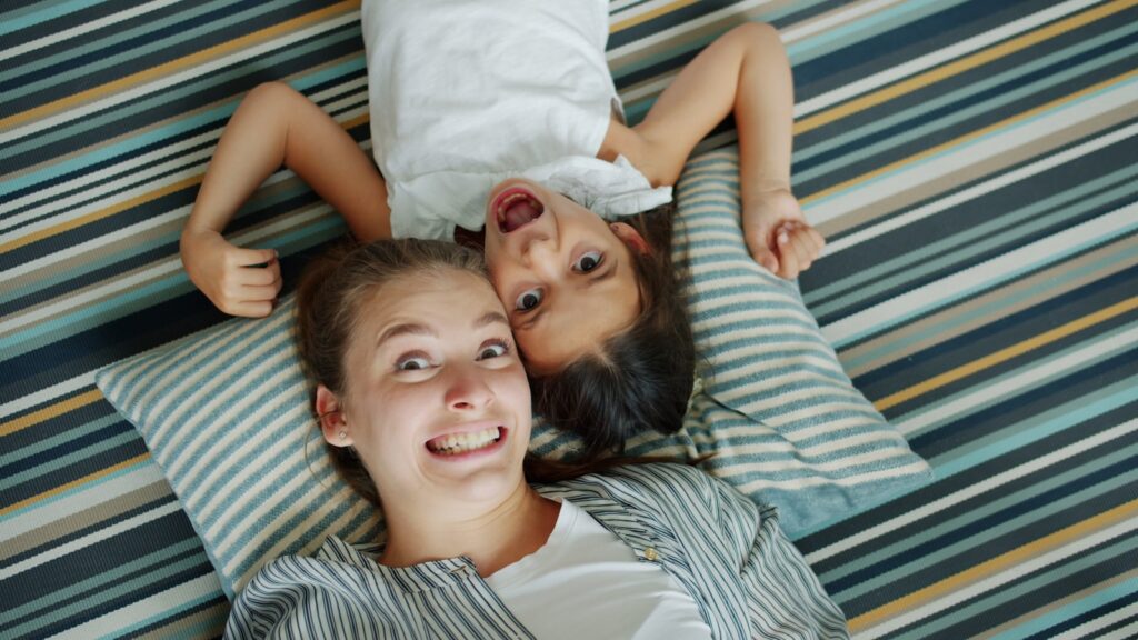Two girls lying on striped floor, making faces.
