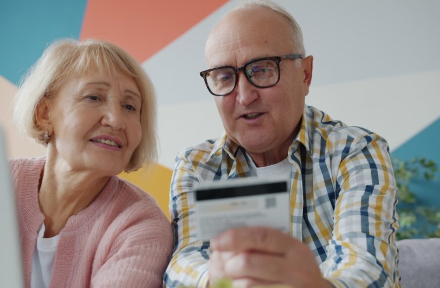 Elderly couple looking at credit card and laptop.