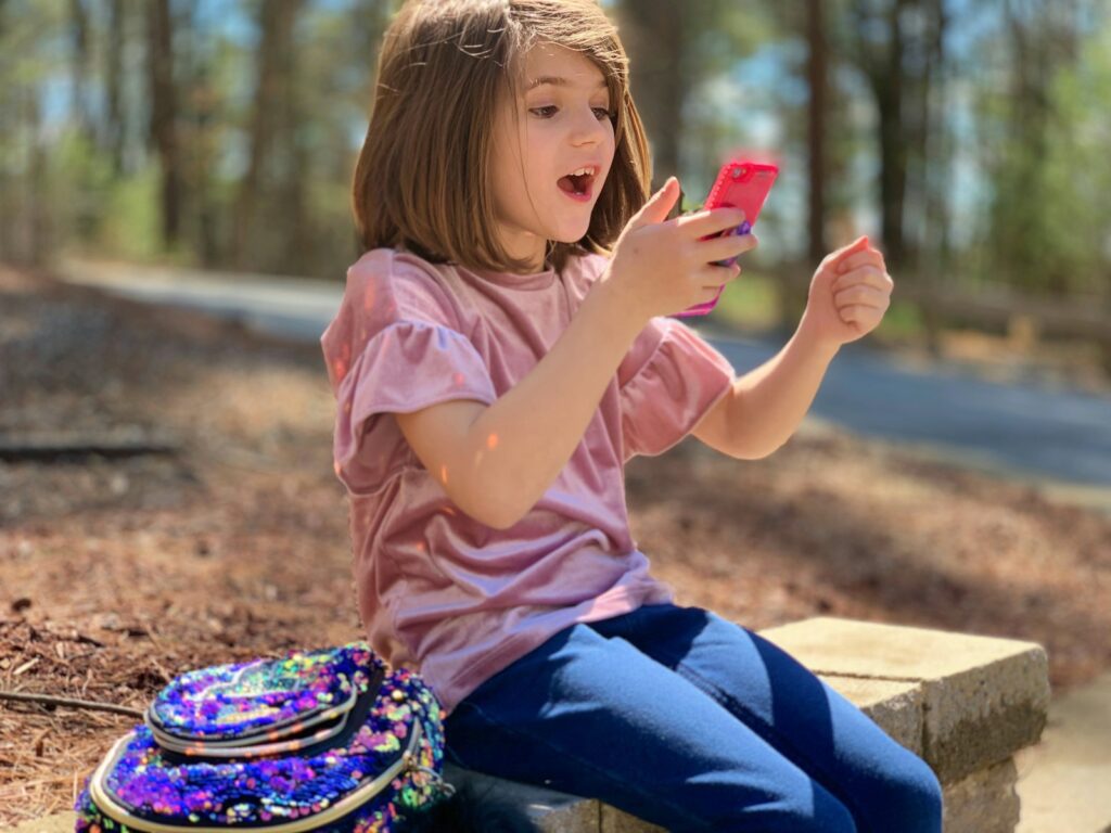 A little girl sitting on a bench using a cell phone