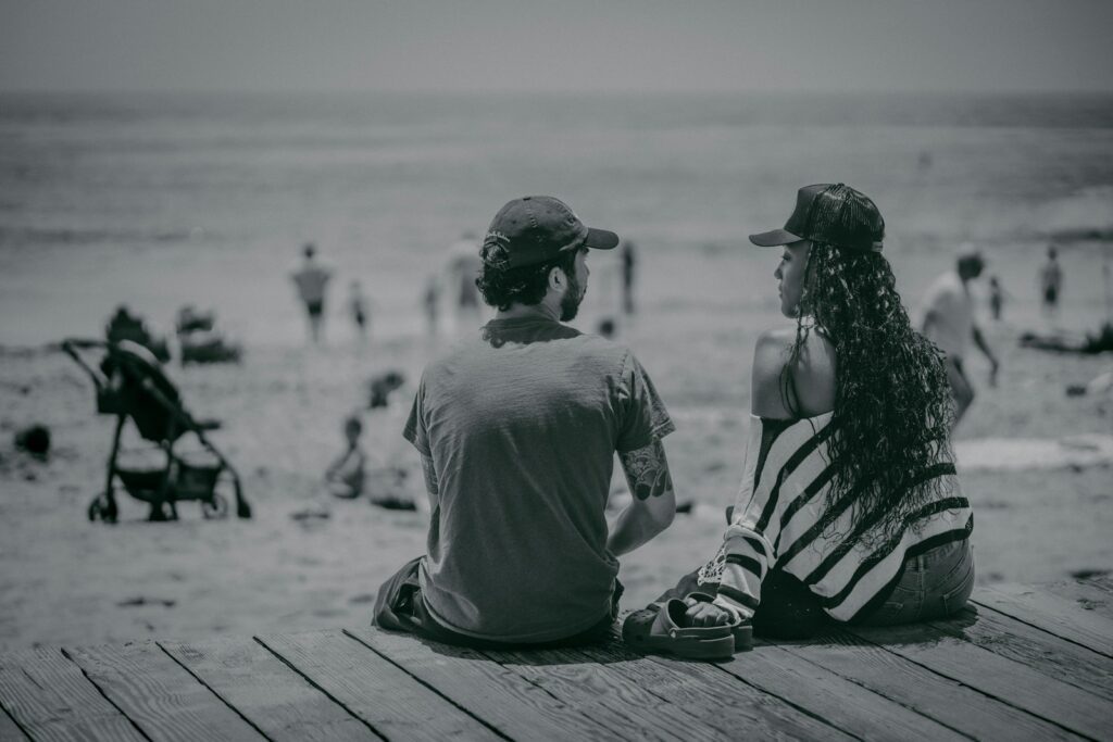 a man and a woman sitting on a pier looking at the beach