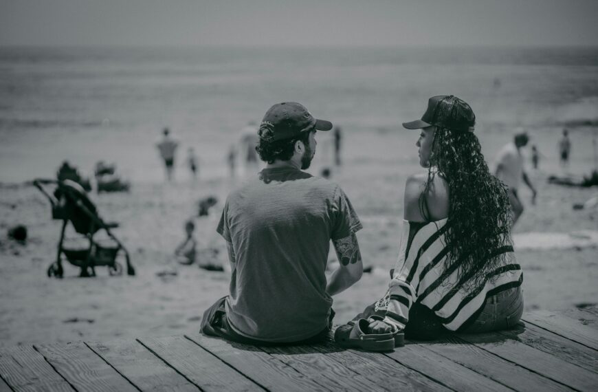 a man and a woman sitting on a pier looking at the beach