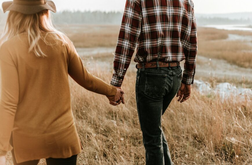 man and woman walking along grass field while holding hands