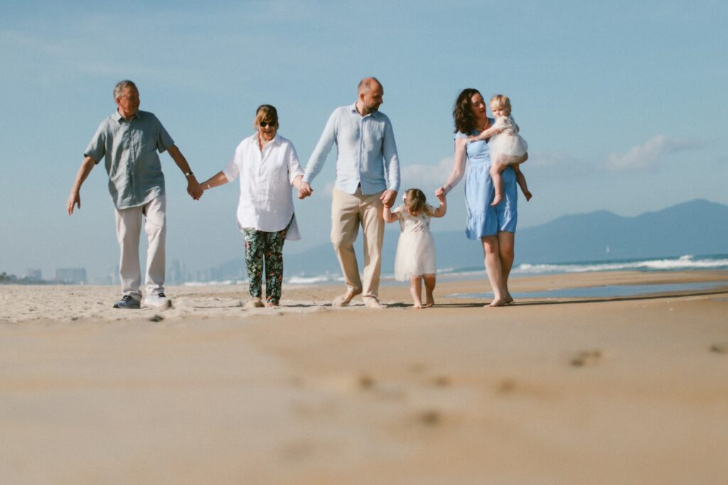 A multi-generational family walks on a sandy beach.