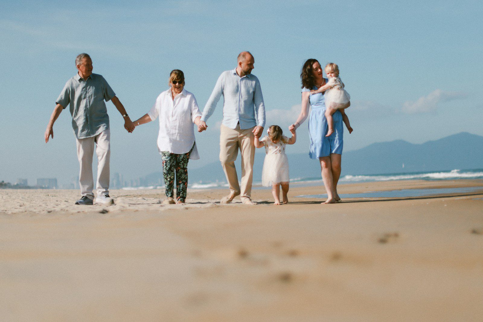 A multi-generational family walks on a sandy beach.