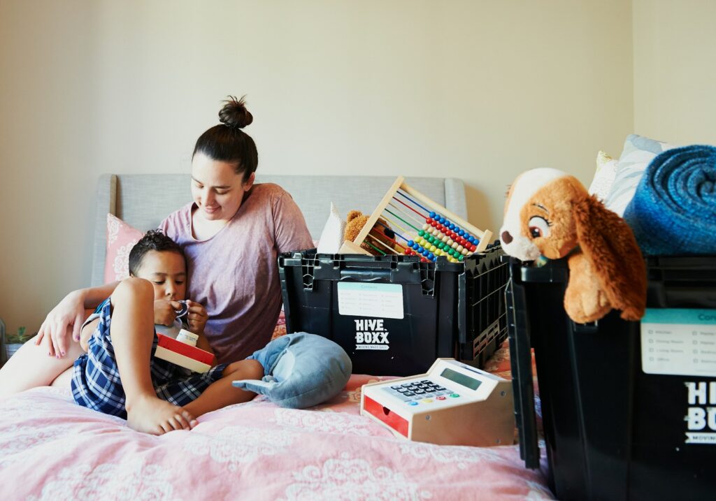 girl in pink shirt sitting on bed beside brown teddy bear