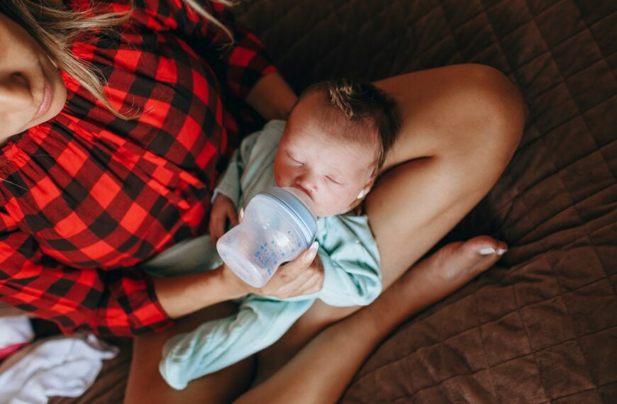 woman in red and black plaid shirt holding baby drinking milk