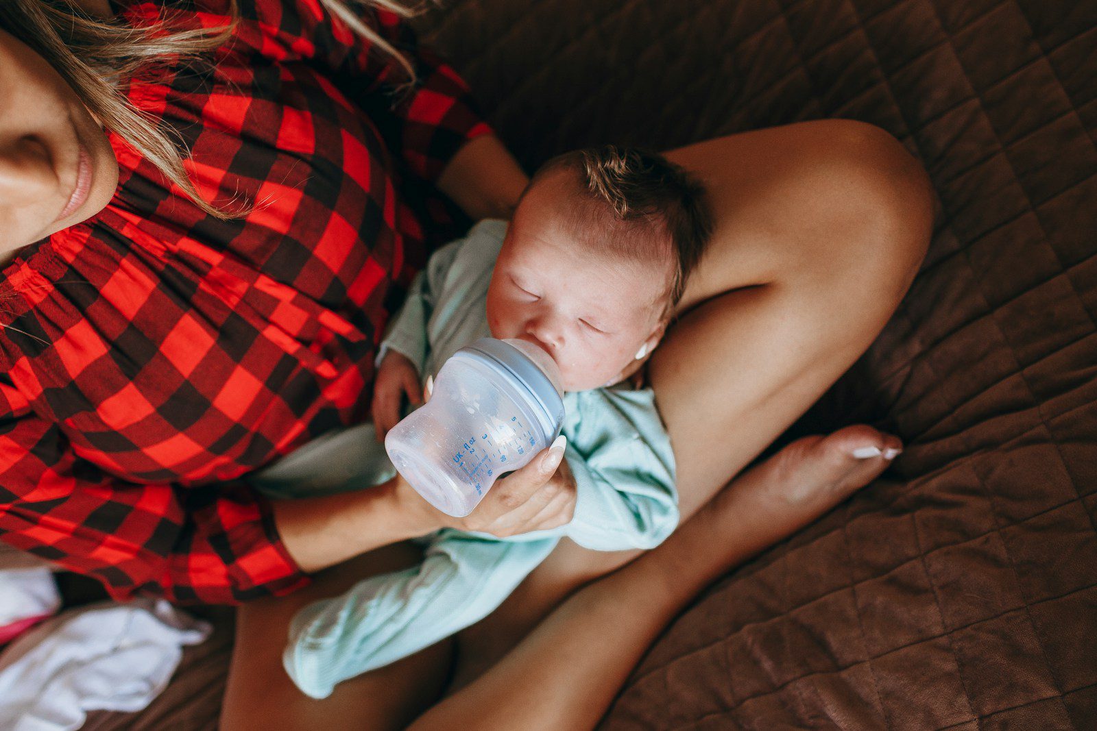 woman in red and black plaid shirt holding baby drinking milk
