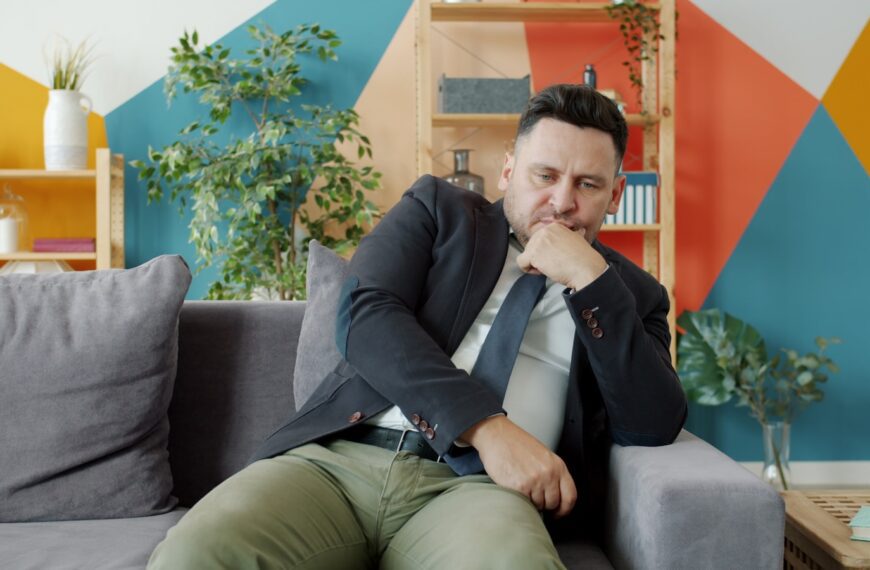 Man in suit sitting on couch looking thoughtful.
