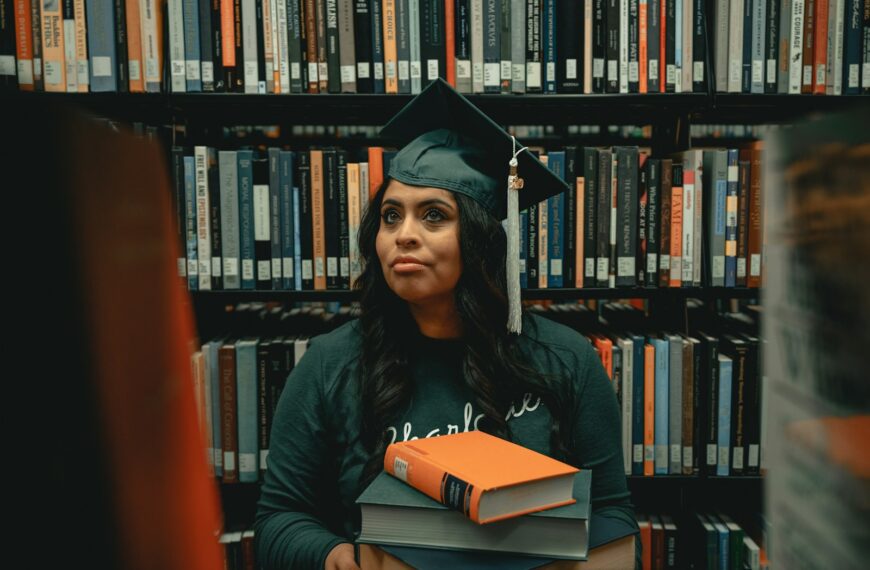 a woman in a cap and gown holding a stack of books