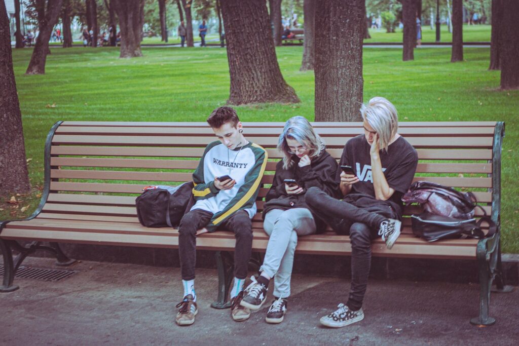 Three friends sitting on a park bench looking at phones.