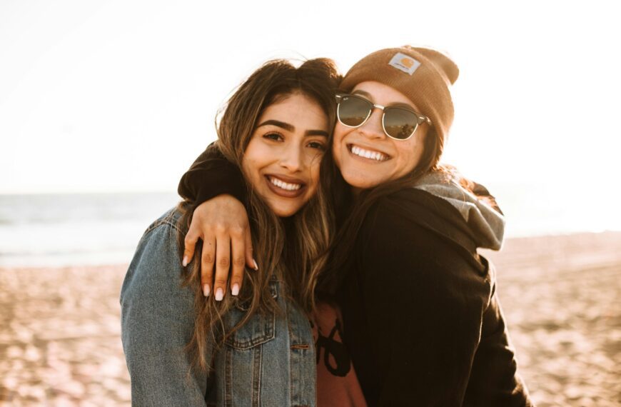 woman hugging other woman while smiling at beach