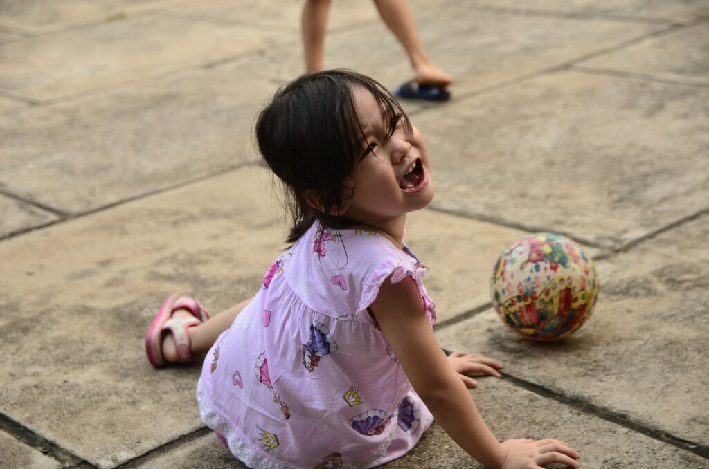 girl in pink and white floral dress sitting on gray concrete floor during daytime