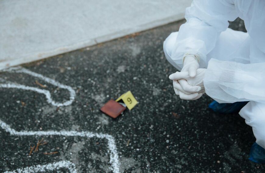 Forensic investigator examines crime scene outline on asphalt in protective suit.