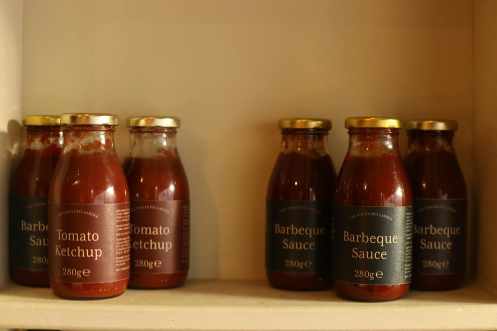 Close-up of ketchup and barbecue sauce bottles neatly arranged on a kitchen shelf.