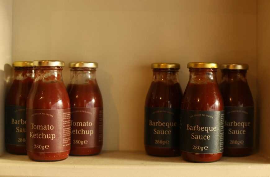 Close-up of ketchup and barbecue sauce bottles neatly arranged on a kitchen shelf.