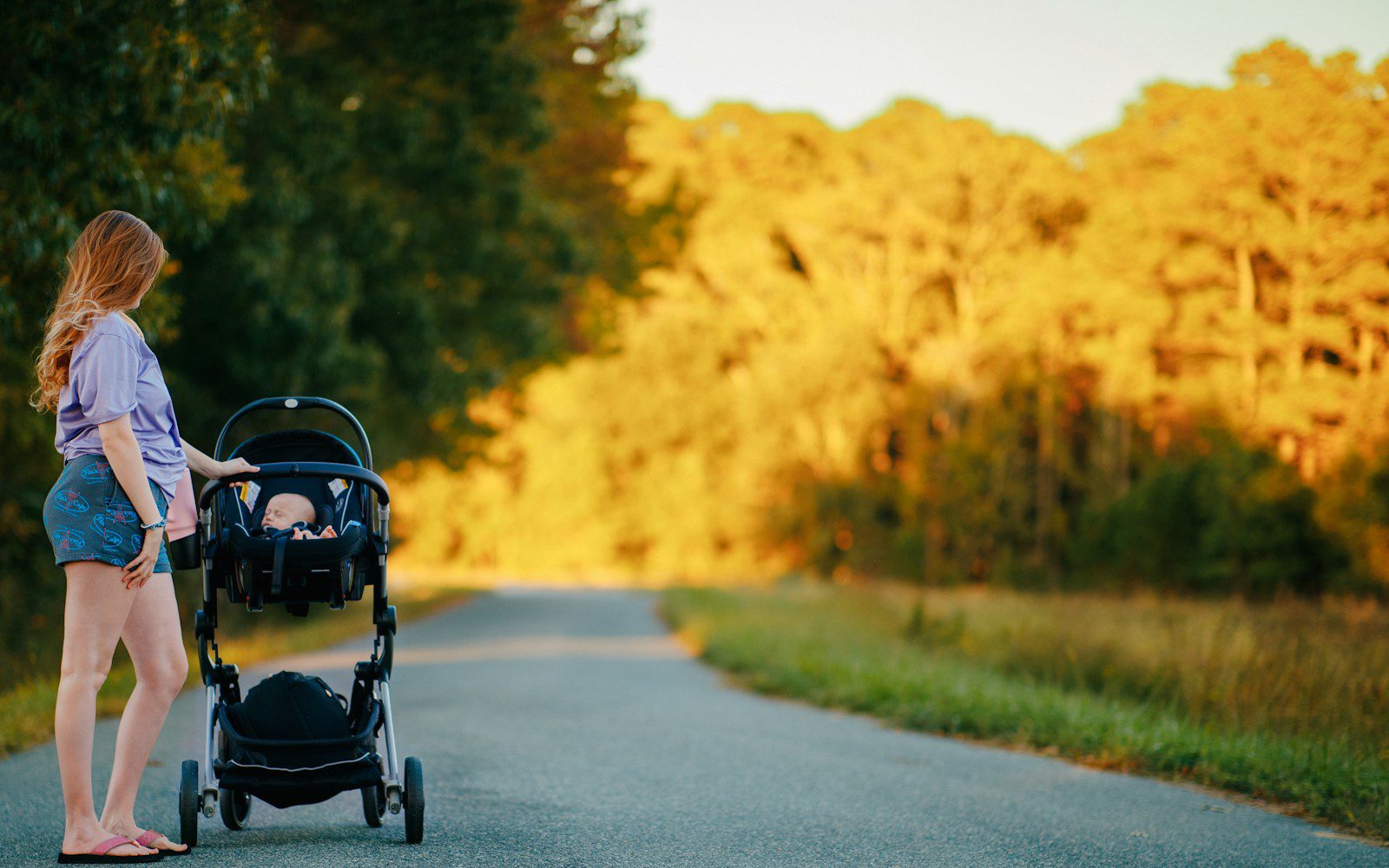 Woman pushing a baby stroller on a country road