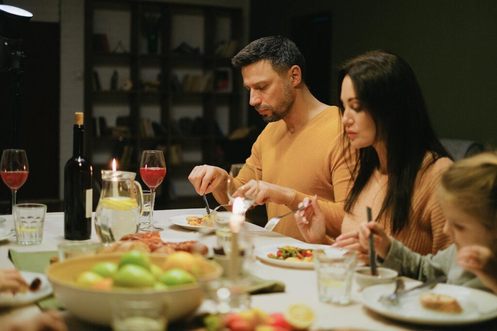 A family gathered around a dinner table indoors, enjoying a meal together with wine and candles.