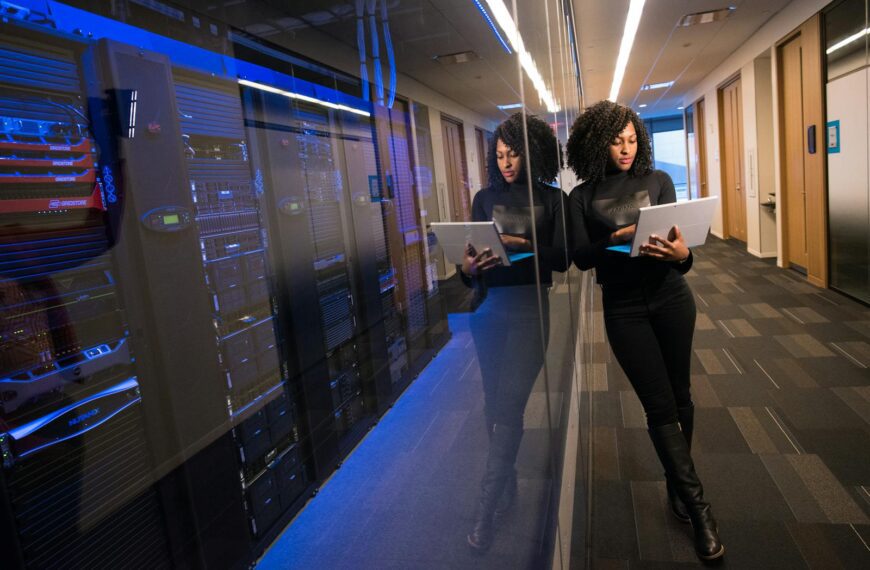 A woman using a laptop navigating a contemporary data center with mirrored servers.