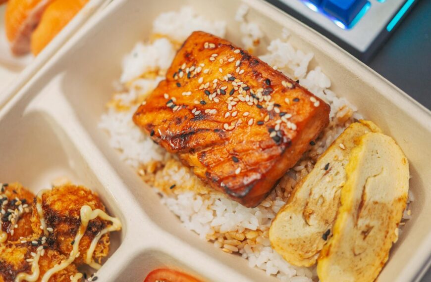 Close-up of a grilled salmon bento box with rice, sesame seeds, and tamago for a delicious meal.
