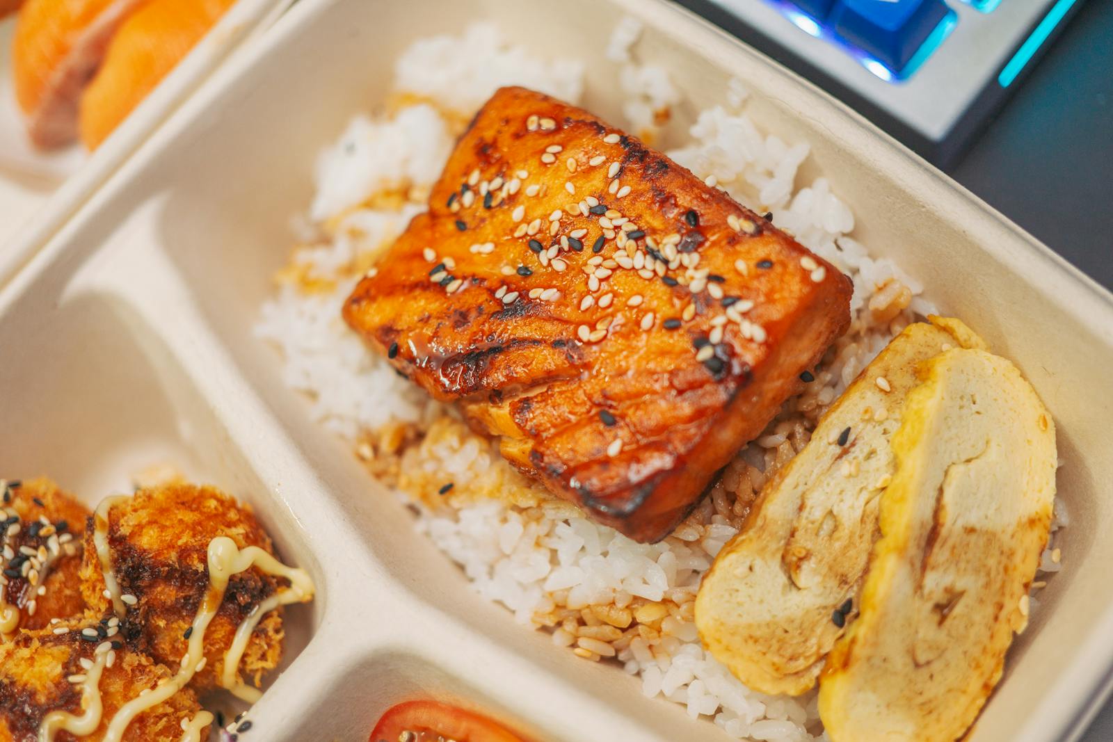 Close-up of a grilled salmon bento box with rice, sesame seeds, and tamago for a delicious meal.