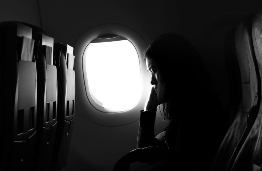 A woman in silhouette sits by an airplane window, experiencing travel journey.